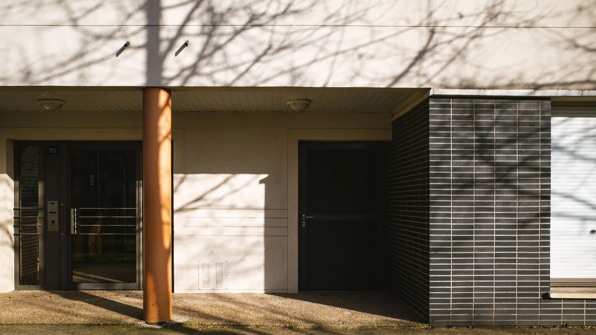 Puerta acristalada del portal de un edificio de viviendas, con el portero automático junto a la entrada