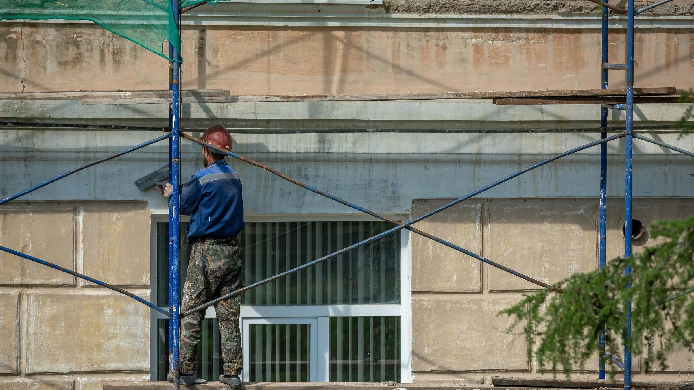 Operario reparando la fachada de un edificio de viviendas subido a un andamio