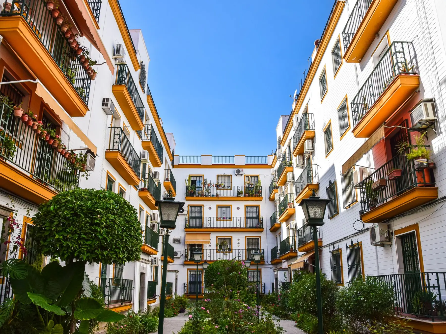 Patio interior ajardinado de una comunidad de vecinos rodeado de fachadas blancas con balcones